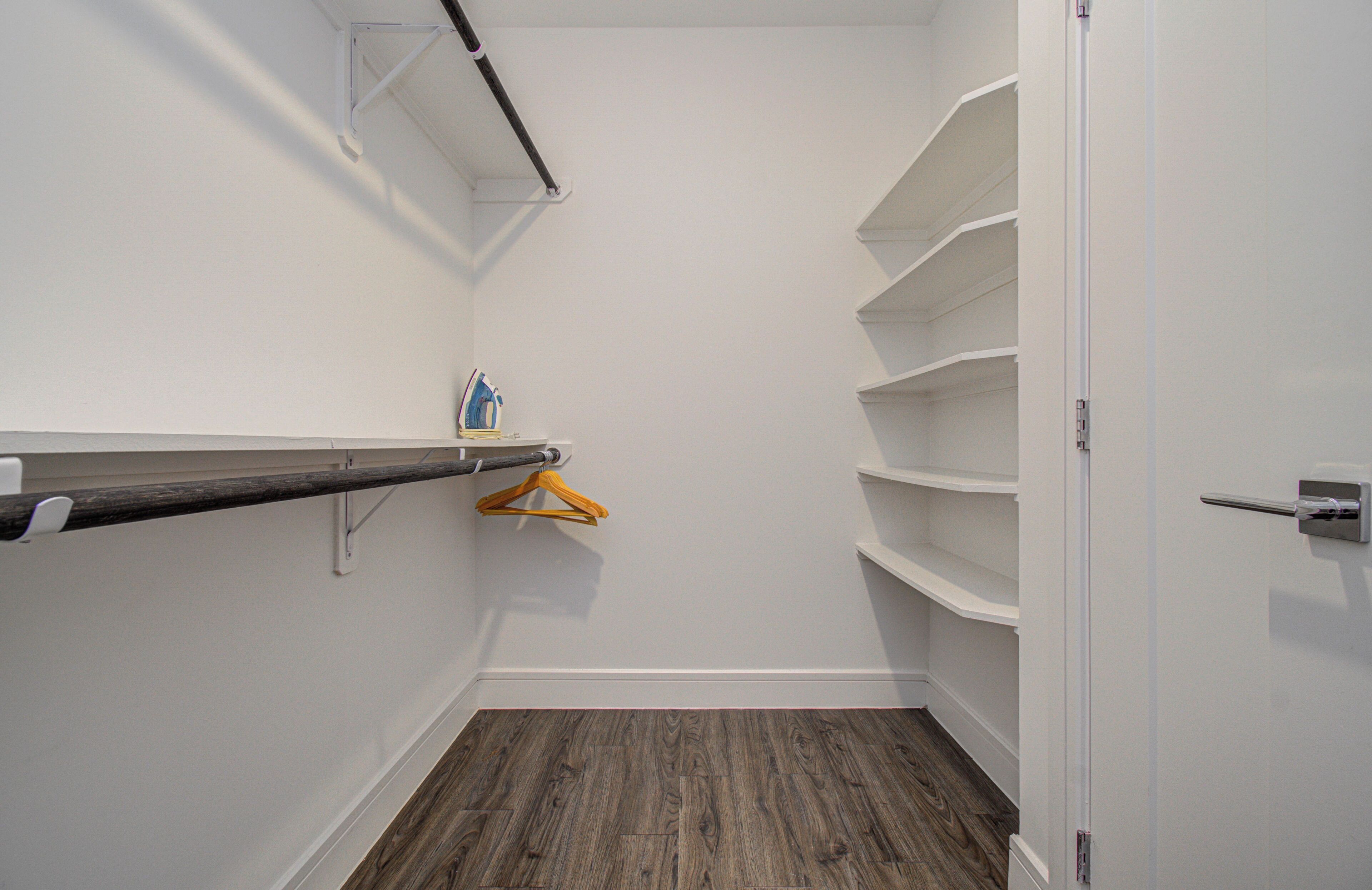 A walk-in closet with wooden flooring, white walls, and built-in shelves.