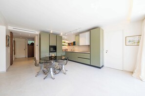 Une cuisine moderne avec un coin repas, comprenant une table et des chaises en verre, des meubles de couleur verte et un plafond blanc.
