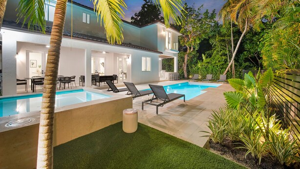 Ein modernes Haus mit Swimmingpool, Sitzgelegenheit im Freien und üppiger Bepflanzung.