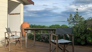 Une terrasse en bois avec deux chaises et une table, donnant sur une étendue d’eau et une zone verdoyante.