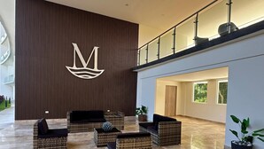 Eine geräumige Lobby mit Korbmöbeln, einem großen Wandlogo und einem Glasgeländer mit Blick ins Innere.