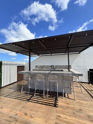 Une terrasse extérieure dotée d’une pergola, d’un comptoir en marbre et de quatre chaises.