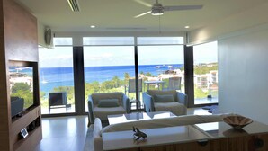 Ein modernes Wohnzimmer mit großem Fenster, Deckenventilator und Blick auf das Meer.