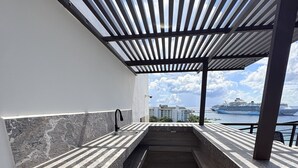 Eine moderne Außenküche mit integriertem Spülbecken, Grill und Blick auf ein Kreuzfahrtschiff im Hintergrund.