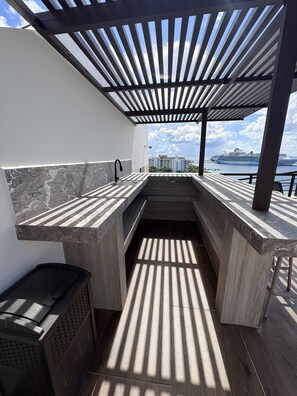 Eine moderne Außenküche mit integriertem Spülbecken, Grill und Blick auf ein Kreuzfahrtschiff im Hintergrund.