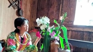 A person seated at a wooden table with a vase of flowers, a teapot, and a bowl. - Dong Que Homestay - Hostel (Ha Giang)
