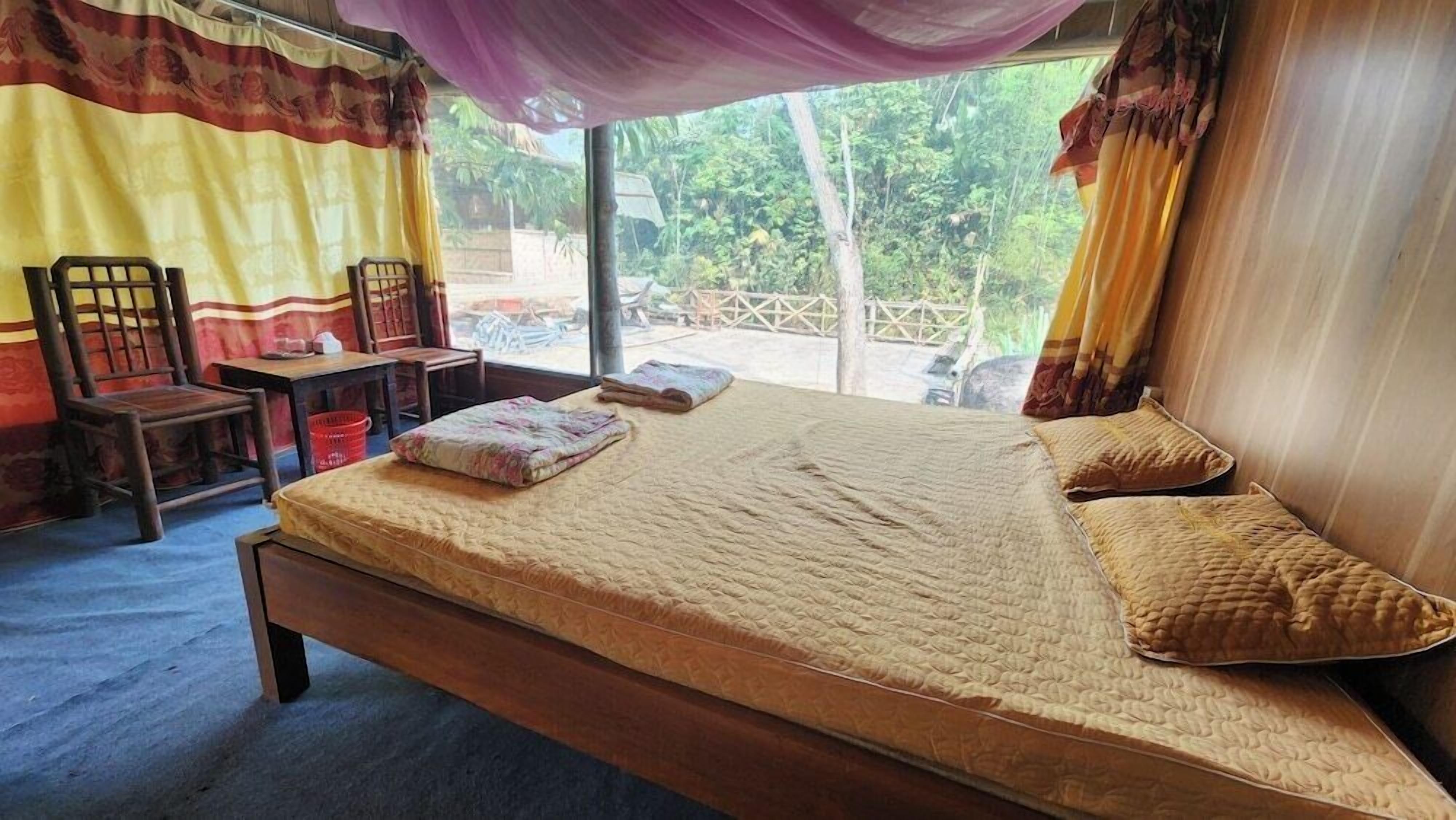 A single bed with a mattress, pillows, and a blanket in a room with a chair and a table.