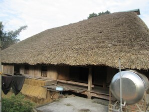 A traditional thatched-roof house with a wooden porch and a metal pot. - Dong Que Homestay - Hostel (Ha Giang)