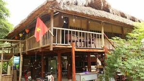 A traditional wooden building with a thatched roof, a balcony, and a flag. - Dong Que Homestay - Hostel (Ha Giang)