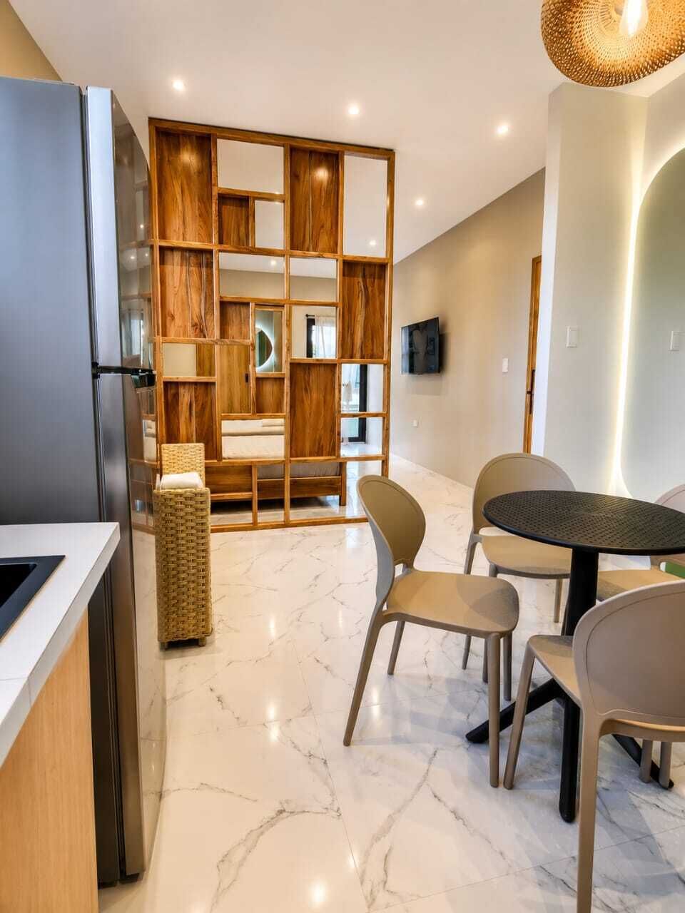 Una cocina moderna con refrigerador empotrado, estanterías de madera y un comedor con mesa redonda y sillas.