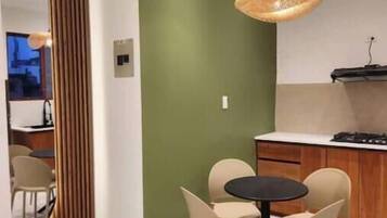 A modern kitchen with a dining area, green accent wall, and a hanging light fixture.