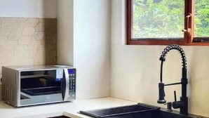 A kitchen with a microwave, sink, and window with a view of greenery.