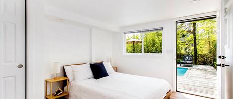A bedroom with a bed, a nightstand, a window, and a view of an outdoor area.