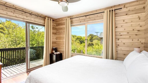 Quarto com cama, ventilador de teto e grandes janelas.