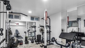 Uma academia com diversos equipamentos de exercício, um banco de supino e um espelho.