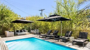 Piscina cercada por vegetação, com espreguiçadeiras e guarda-sóis.