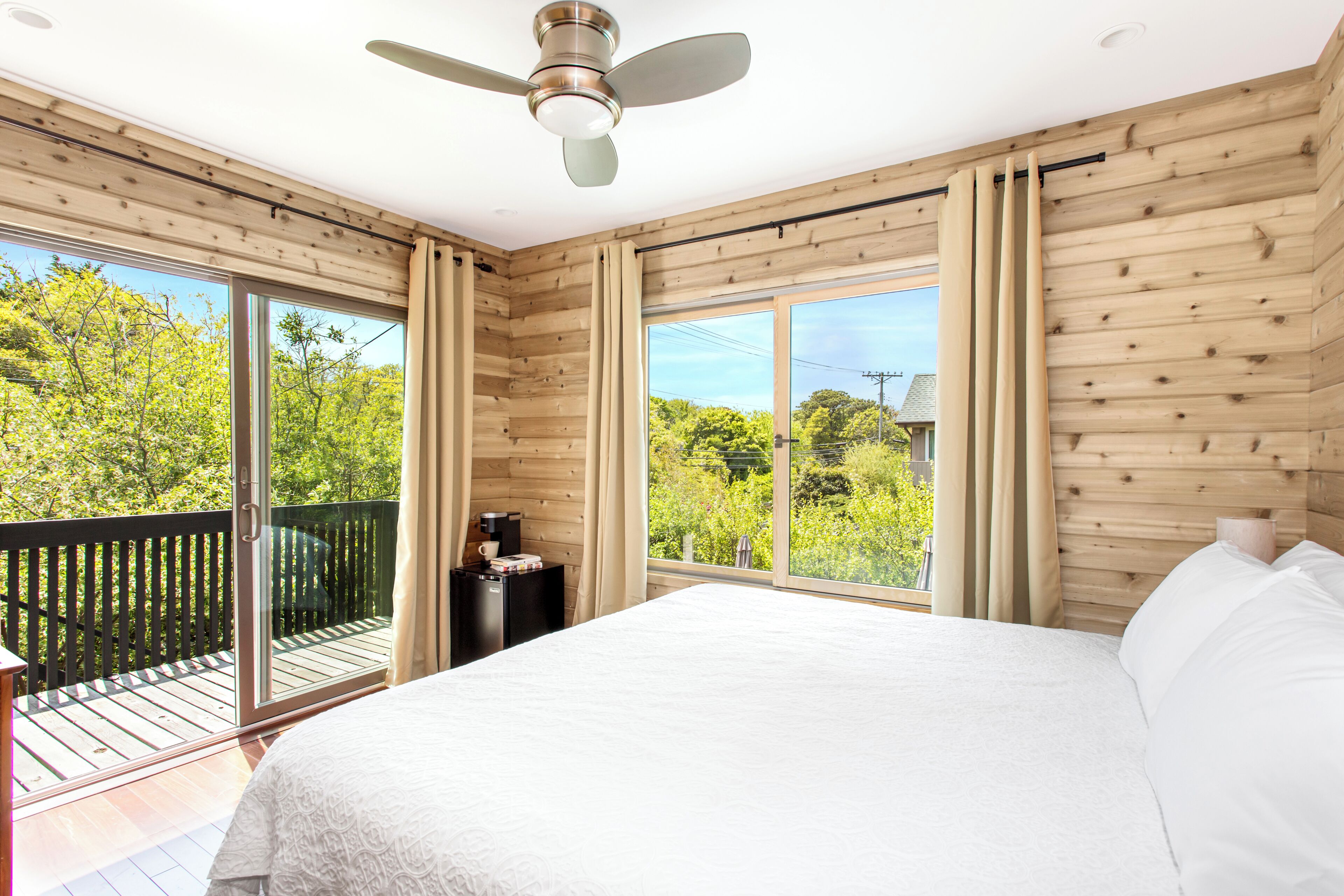Een slaapkamer met een groot bed, een plafondventilator en een balkon met uitzicht op bomen.