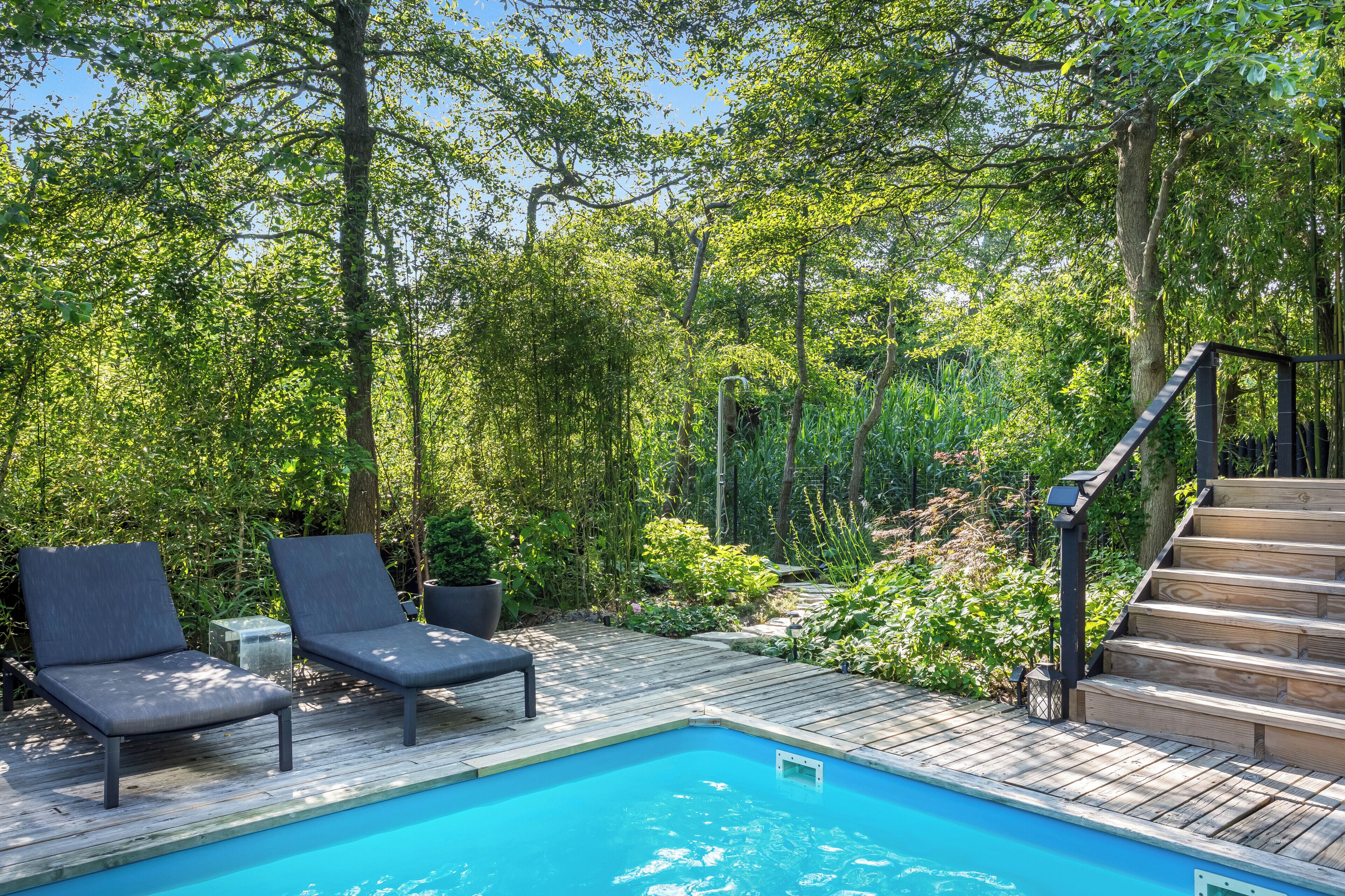 A pool area with wooden deck, two lounge chairs, and a staircase leading to a higher level.