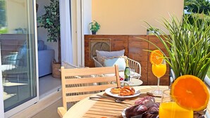 Ein Essbereich im Freien mit einem Tisch, der für das Frühstück gedeckt ist, darunter Croissants, Obst und Getränke.