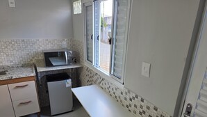 A compact kitchen with a microwave, refrigerator, and a window with blinds.
