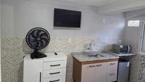 A kitchen with a tiled backsplash, a microwave, a sink, a fan, and a TV mounted on the wall.
