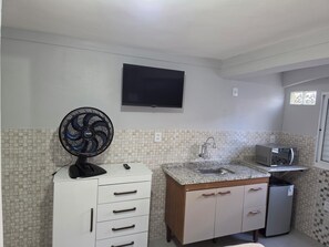 A kitchen with a tiled backsplash, a microwave, a sink, a fan, and a TV mounted on the wall.