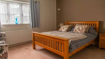 Un dormitorio con cama de madera, ventana con cortinas, radiador y mesita de noche con lámpara.