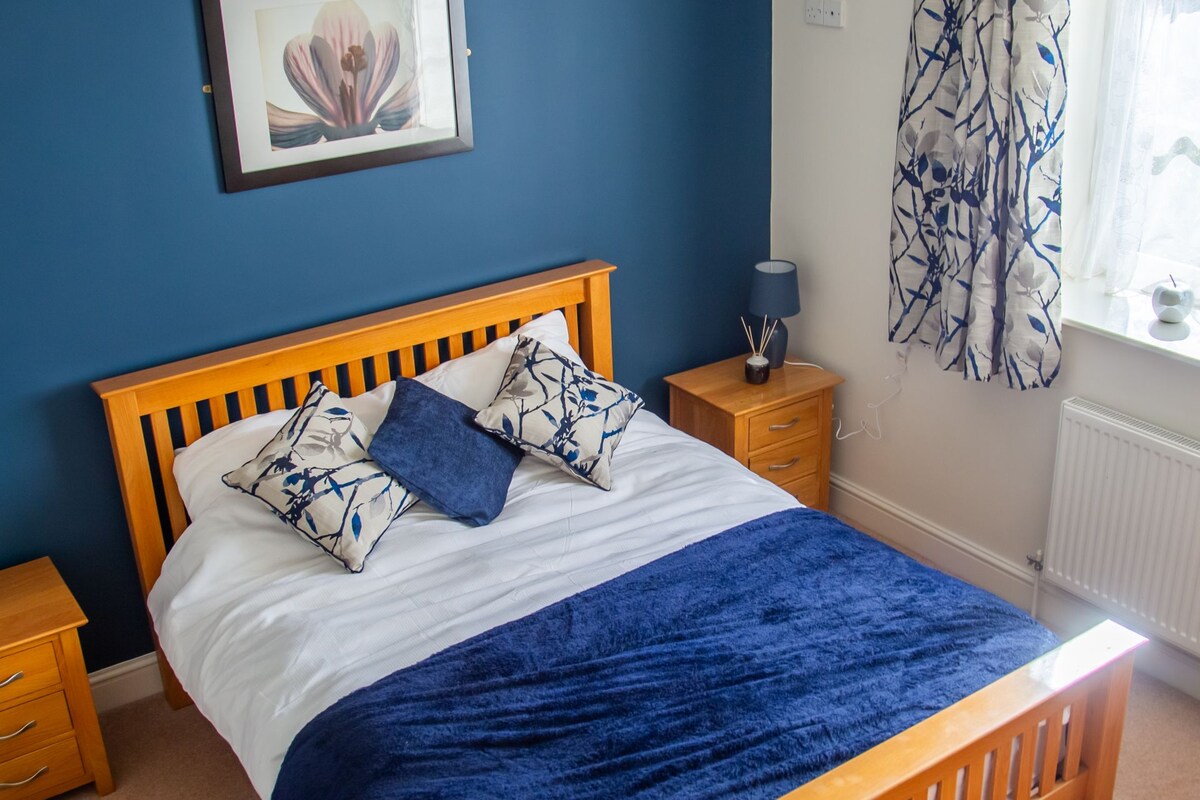 Un dormitorio con cama de madera, una mesita de noche, una lámpara, un cuadro en la pared y una ventana con cortinas.