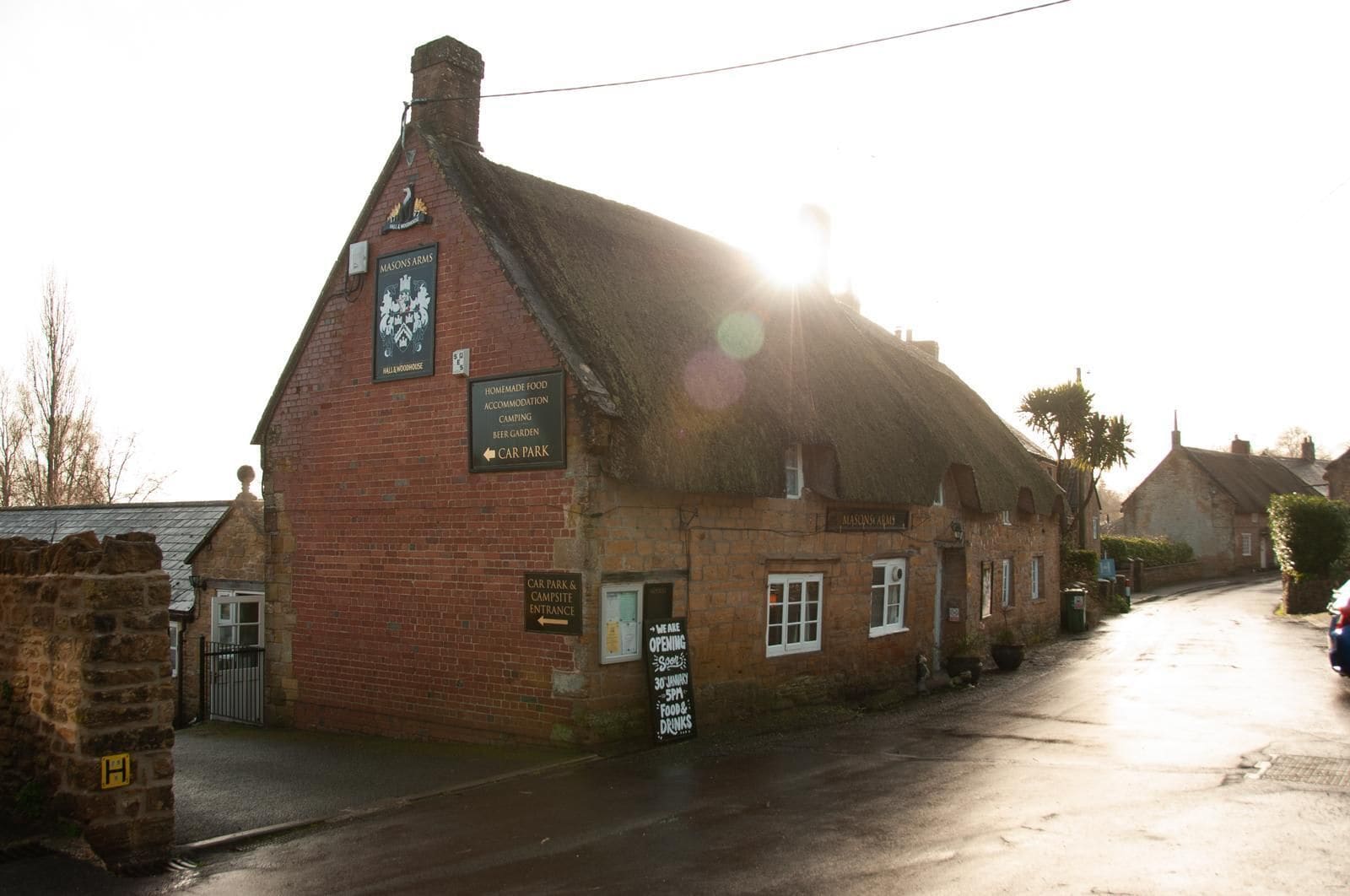 A traditional building with a thatched roof, signs indicating it offers homemade food, accommodation, camping, and a beer garden.