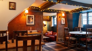 A cozy pub with wooden furniture, a fireplace, and string lights.