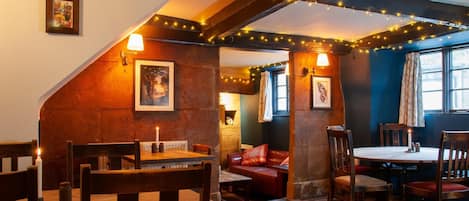 A cozy pub with wooden furniture, a fireplace, and string lights.