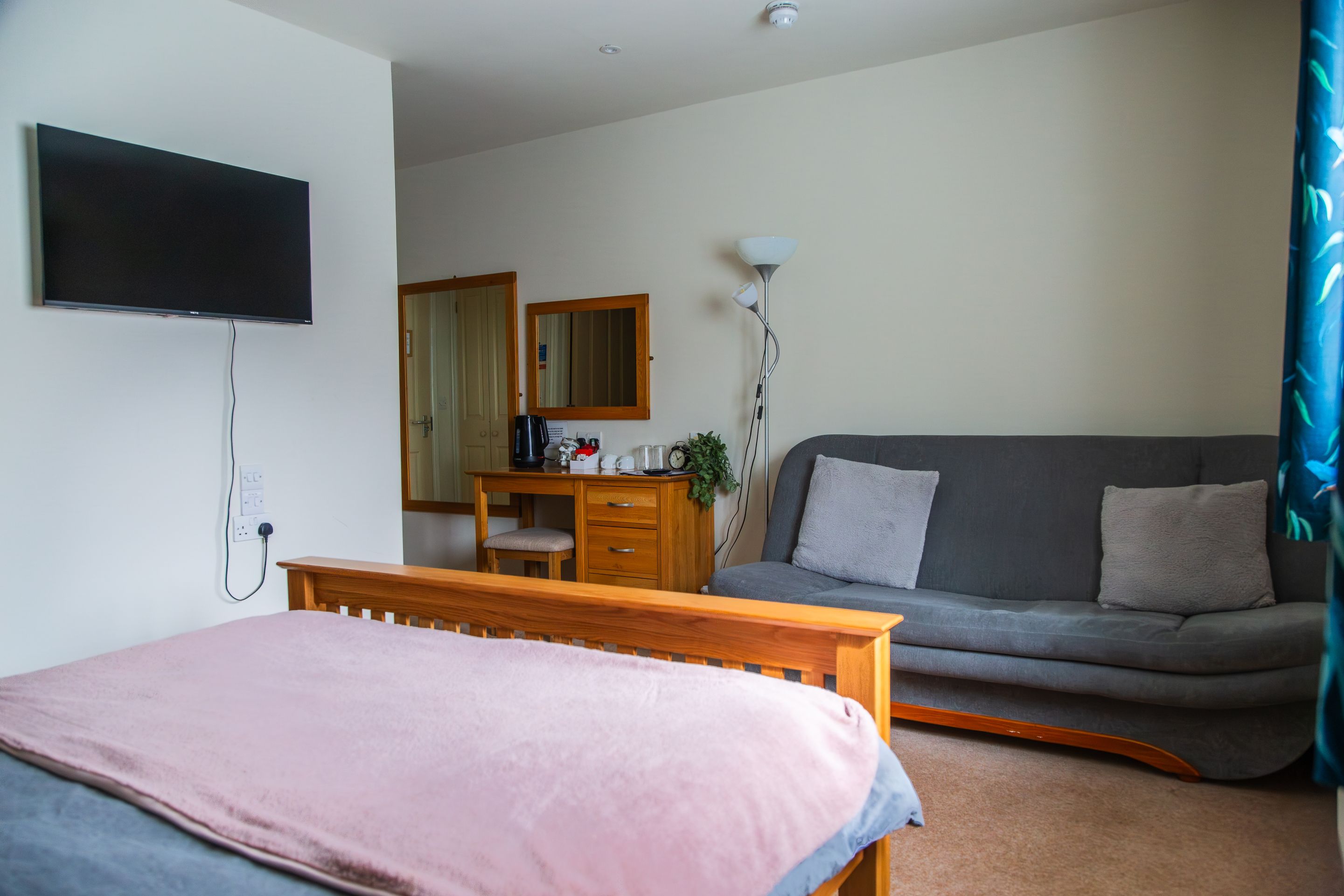 A bedroom with a bed, a desk, a sofa, a TV, and a mirror.