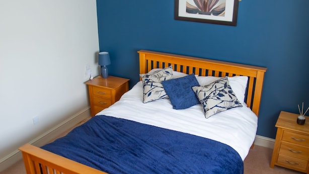 A bedroom with a wooden bed, a blue wall, a ceiling fan, and a framed picture on the wall.
