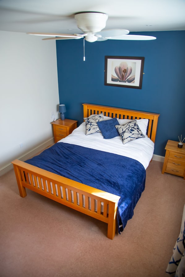 Un dormitorio con cama de madera, pared azul, ventilador de techo e imagen enmarcada en la pared.