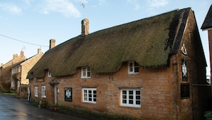 A traditional stone building with a thatched roof, a signboard, and a window with a white frame.