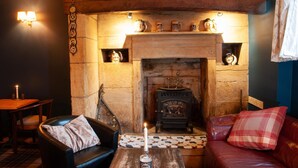 A cozy room with a stone fireplace, a leather sofa, a wooden table, and a small table lamp. - The Masons Arms (Odcombe)