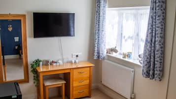 A bedroom with a bed, a desk, a chair, a television, a ceiling fan, and a window with curtains.