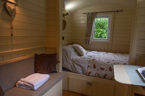 A cozy bedroom with a bed, a window with curtains, a bedside table, and a heart-shaped decoration on the wall.