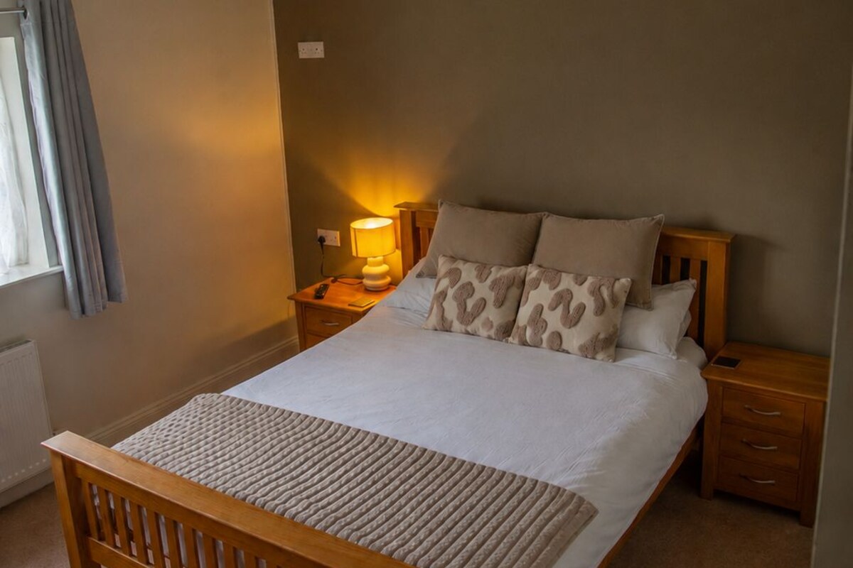 Un dormitorio con una cama de madera, un ventilador de techo, una lámpara de noche y una ventana con cortinas.