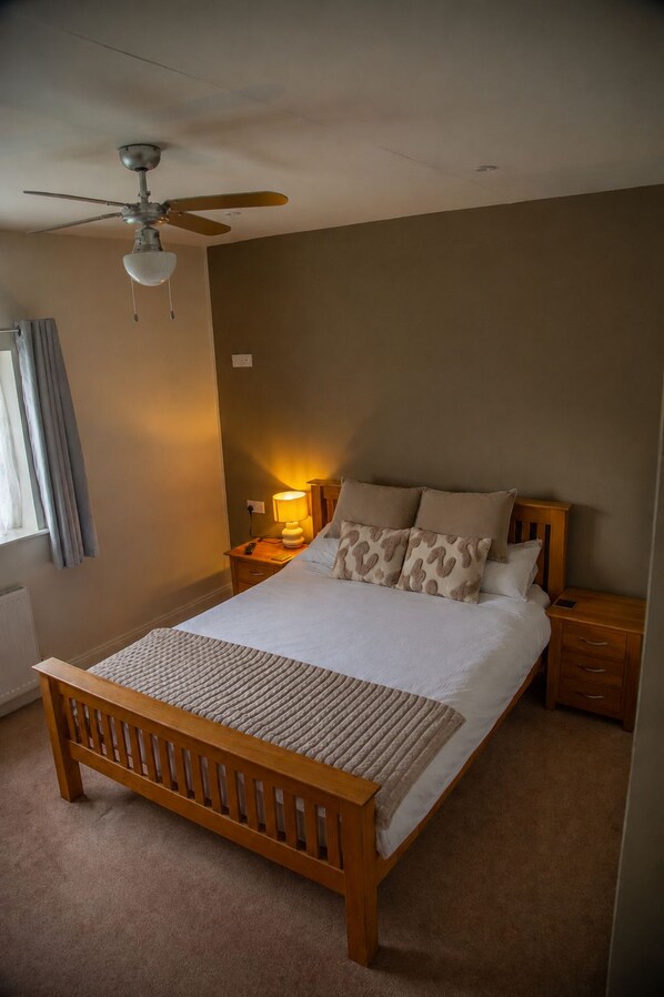 Une chambre à coucher avec un lit en bois, un ventilateur de plafond, une lampe de chevet et une fenêtre avec des rideaux.