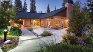 A modern building with a brick chimney, a covered patio with seating, and a pathway leading to the entrance.