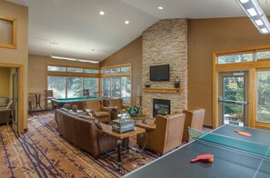 A living room with a pool table, leather sofas, and a stone fireplace.