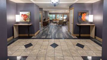 A hotel hallway with a modern design, featuring a geometric patterned floor, a chandelier, and artwork on stands.