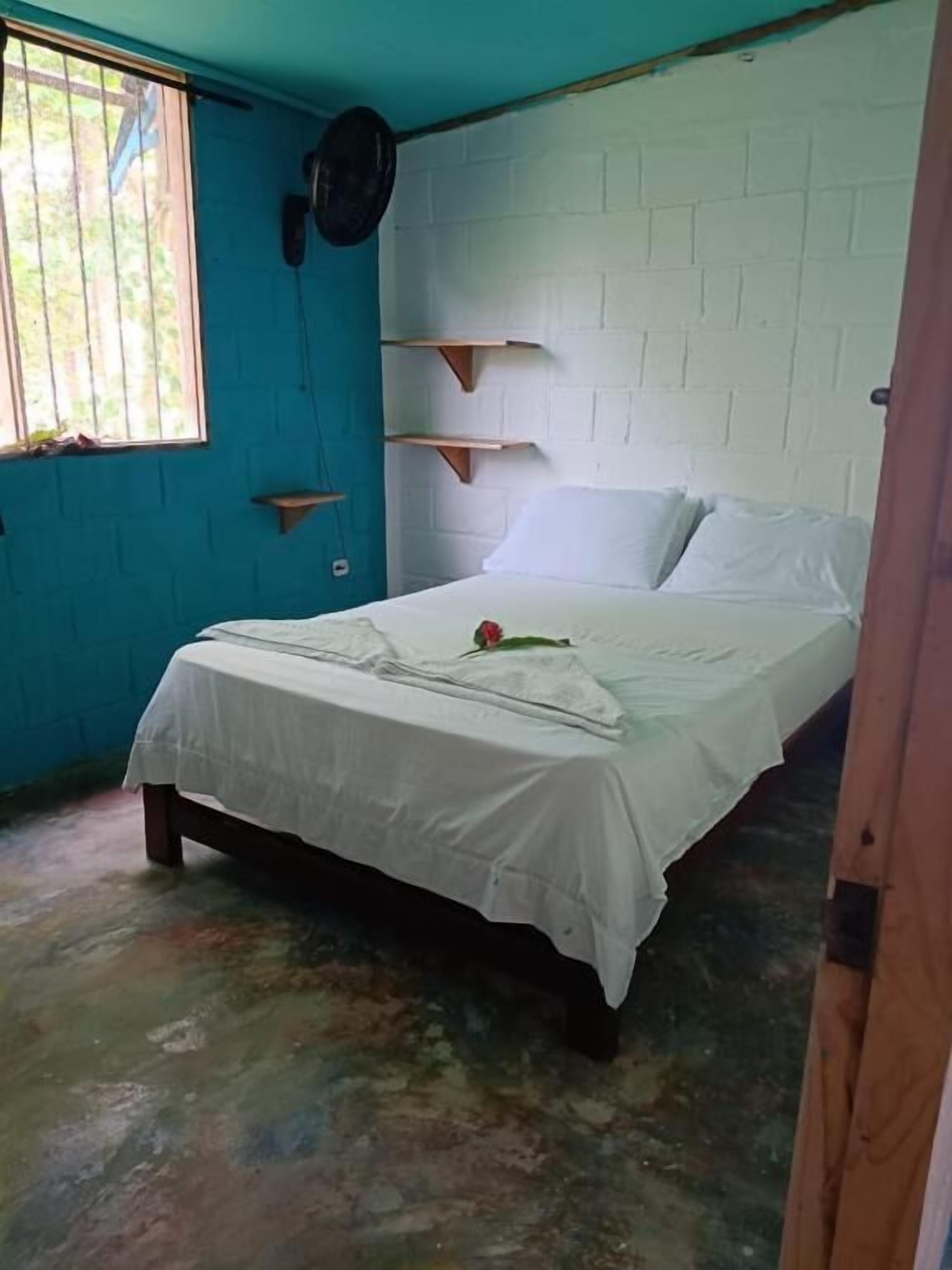 A room with a bed, a window with bars, a white brick wall, and a blue wall.
