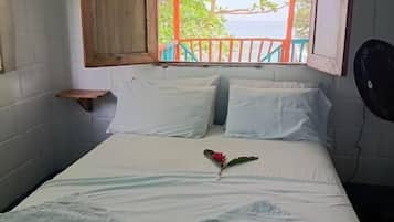 A single bed with white linens, a wooden headboard, and a window with an open shutter.