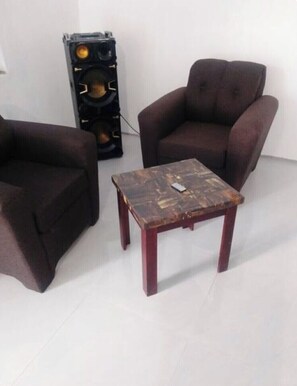 A room with a brown armchair, a wooden coffee table, and a speaker unit.