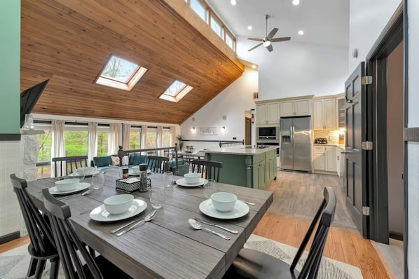 A spacious dining area with a high ceiling and skylights, a kitchen with modern appliances, and a view of the outdoors. - 5BR Private Hot Tub, Movie Theater, Game Room! (East Stroudsburg)