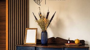 Un mueble azul oscuro con un jarrón de flores secas y un cuadro enmarcado encima.