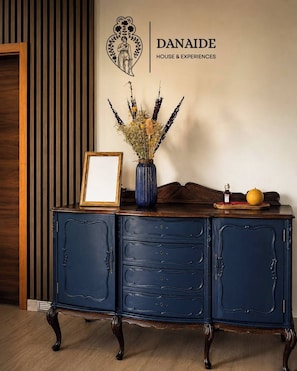 Un meuble bleu foncé sur lequel sont posés un vase de fleurs séchées et un tableau encadré.