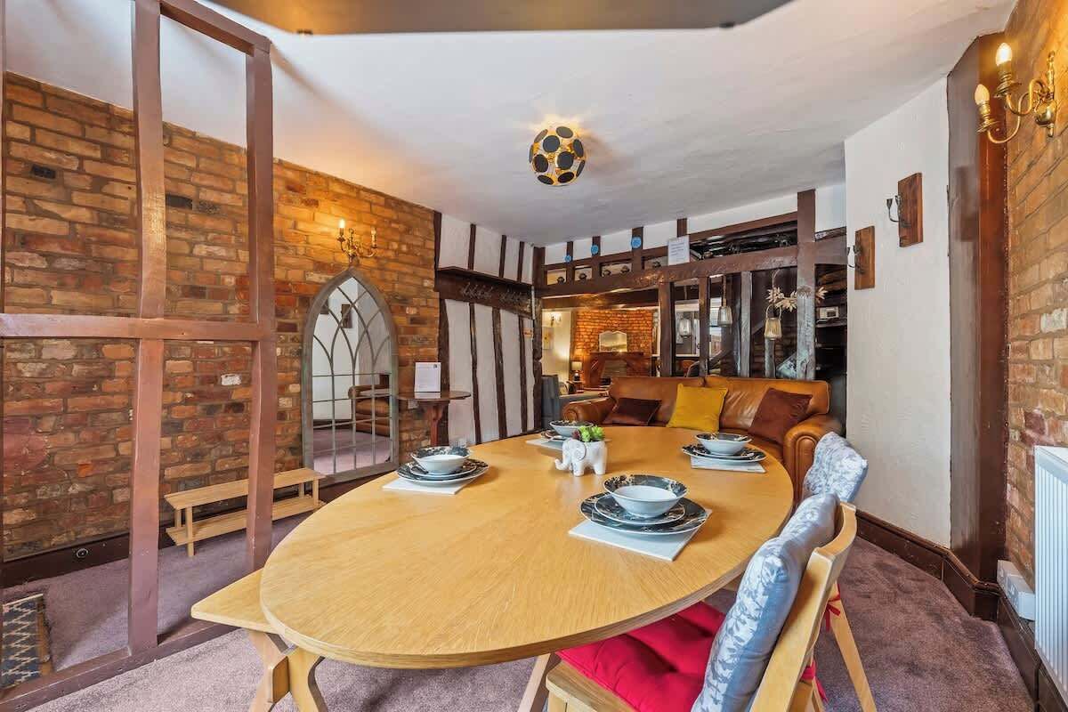 A dining area with a round wooden table, chairs, and a brick wall.